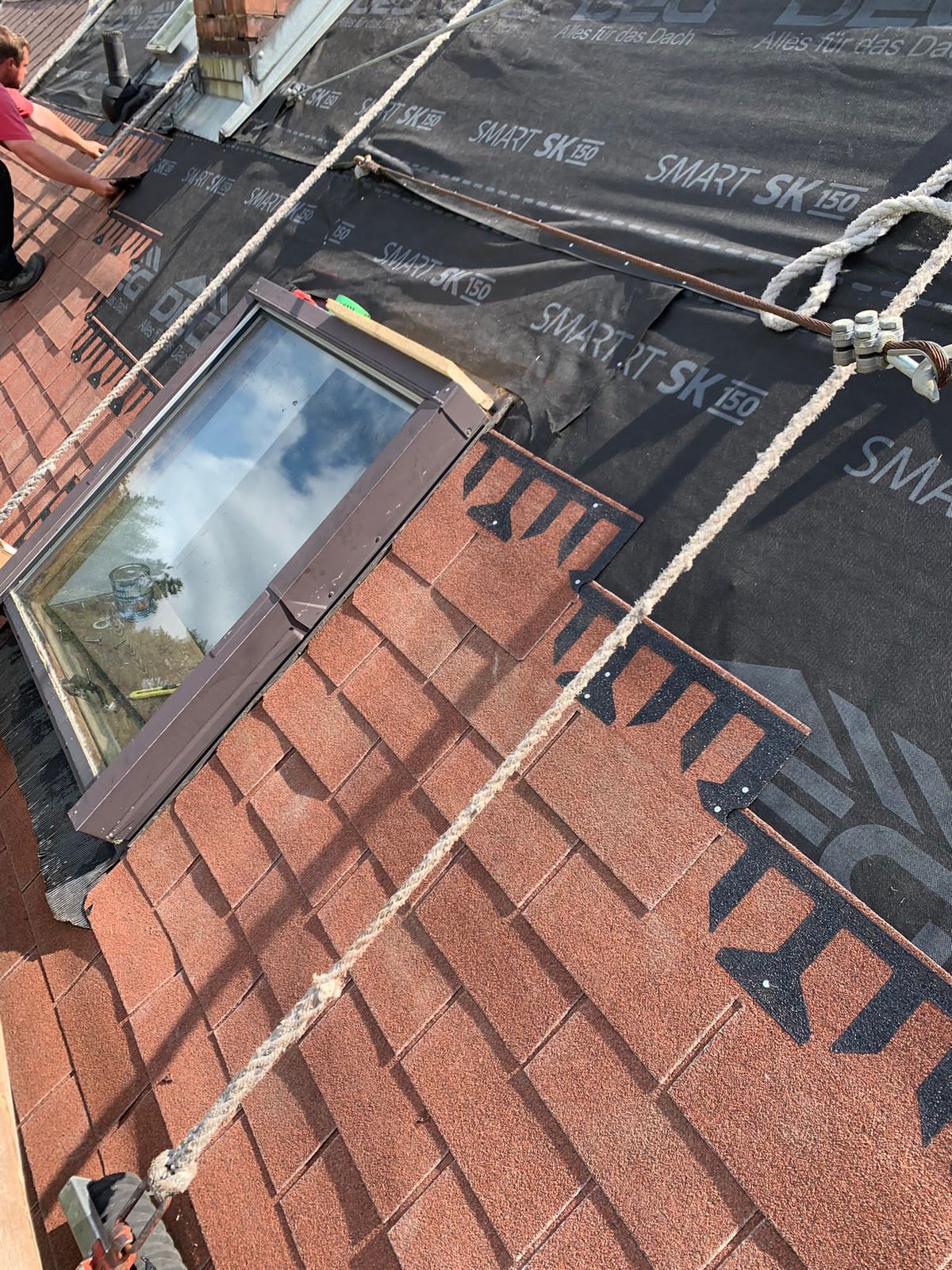 Mitarbeiter deckt rund um ein Dachfenster mit Schindeln ein