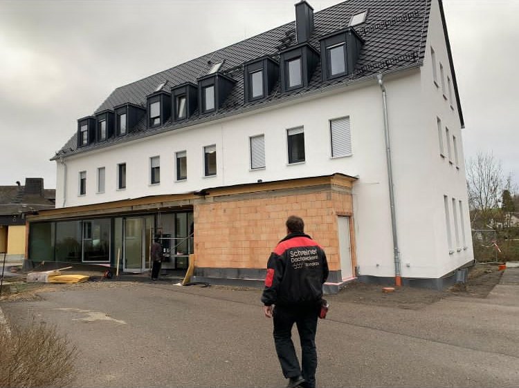 Mehrfamilienhaus mit neu eingedecktem Dach und Gauben, davor ein Mitarbeiter